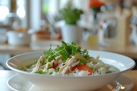 Asian chicken soup with rice noodles, shredded meat, fresh herbs and vegetables in white bowl. Selective focus on traditional Asian cuisine.