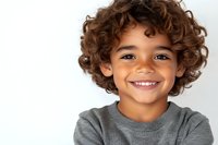 Cheerful mixed-race boy with curly brown hair and bright smile wearing grey sweater against white background, portrait orientation for advertising and lifestyle design.