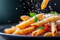 Penne pasta with tomato sauce and parmesan cheese sprinkled from above, garnished with fresh basil leaves. Close-up macro shot with dark background.