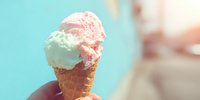 Refreshing ice cream cone with mint and strawberry scoops against turquoise summer background, held by hand in warm sunlight.