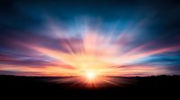Dramatic sunset with vibrant rays of light bursting through dark clouds, creating a spectacular natural light show over silhouetted horizon landscape.