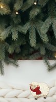 Festive evergreen branches with warm lights and cute sheep ornament on white textured surface, perfect for holiday greeting cards and seasonal marketing materials.
