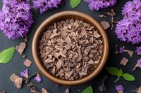 Chocolate chips in ceramic bowl surrounded by fresh lilac flowers on dark background. Sweet baking ingredients and spring floral composition for dessert making.