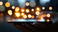 Glowing magical light spheres floating above smartphone in dark, creating ethereal bokeh effect. Hand holds modern device displaying luminous orbs.
