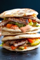 Grilled meat and vegetable panini sandwiches stacked with peppers, lettuce and sauce on dark background for restaurant menu and food advertising.