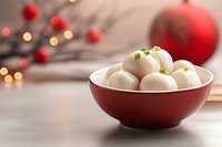 White chocolate truffles in red ceramic bowl with festive holiday decorations and bokeh lights in background, selective focus on homemade candies.