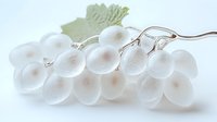 Delicate white glass grapes on silver stem with soft green leaf, artistic still life on light background showing translucent ethereal quality and craftsmanship.