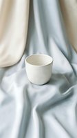 Empty white ceramic cup on draped neutral fabric background, suitable for product mockups, tableware design, and commercial beverage packaging presentations.