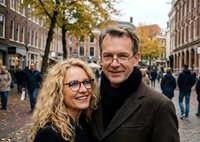 Happy mature Caucasian couple with glasses smiling on autumn city street with fallen leaves and historic brick buildings in background for lifestyle content.