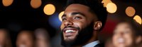 Young African American businessman smiling confidently at corporate event with warm bokeh lights creating elegant atmosphere for professional networking.