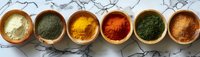 Colorful aromatic spices in clay bowls arranged in row on marble background, including turmeric, paprika, herbs and curry powder. Fresh cooking ingredients.