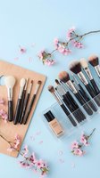 Professional makeup brushes collection with pink cherry blossoms on pastel blue background for beauty and cosmetics applications.