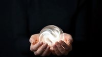 Hands holding glowing crystal ball against dark background, fortune telling and mystical divination concept for spiritual guidance and future prediction.