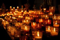 Glowing prayer candles in glass holders creating atmospheric warm light in dark church interior for spiritual contemplation.