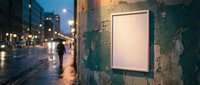 Empty white poster frame on weathered urban wall during rainy evening with blurred city street lights and pedestrian silhouette in background.