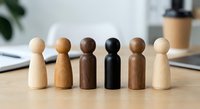 Diverse wooden peg people figures in various skin tones standing together on desk representing teamwork, inclusion and unity in workplace setting.