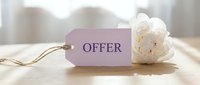 Elegant lavender price tag with the word Offer on a wooden surface beside a white peony flower, soft light background for retail and marketing use.