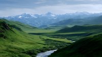 Majestic mountain landscape with winding river flowing through green valley, dramatic peaks rising in distance under blue summer sky and scattered clouds.