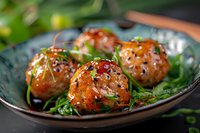 Asian glazed meatballs garnished with sesame seeds and green onions served on ceramic plate with fresh herbs, close up view of appetizing dish.