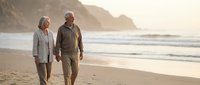 Happy senior couple walking hand in hand on sandy beach at sunset with ocean waves and coastal cliffs in background for retirement lifestyle concepts.