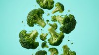 Fresh broccoli florets suspended in mid-air against turquoise background, ideal for healthy eating, nutrition, cooking, and food photography projects.