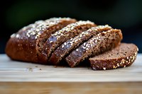 Fresh sliced dark rye bread with sesame and poppy seeds on wooden cutting board, close-up view showing soft texture and crispy crust in natural light.