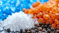 Colorful assortment of various spices and seasonings including sea salt crystals, black peppercorns, and pink Himalayan salt on dark background, macro food photography.