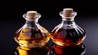 Two elegant glass bottles with cork stoppers containing golden and amber liquids on dark background for aromatherapy essential oils cosmetic products.