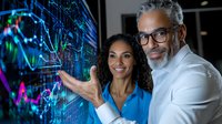 Diverse business team analyzing financial data on digital screen. African American woman and mature man with gray hair discuss market trends and charts.