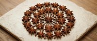 Star anise spices arranged in decorative circular mandala pattern on white ceramic plate, aromatic cooking ingredients for culinary and kitchen use.