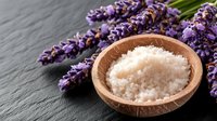 Fresh sea salt in wooden bowl with aromatic lavender flowers on dark stone background, spa wellness concept for natural cosmetics and body care.