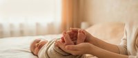 Tender moment of parent gently holding newborn baby feet in warm sunlit nursery room. Soft natural lighting creates peaceful family bonding atmosphere.