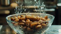 Fresh almonds splashing in clear water in glass bowl on marble counter, dynamic food photography with water drops and motion capture for healthy eating concept.