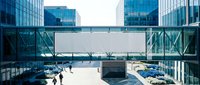 Blank billboard banner on glass bridge between modern corporate office buildings, people walking below, blue sky, urban business district.