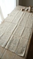 Natural linen fabric laid flat on rustic wooden table near window with soft daylight, craft supplies and twine spool, organic textile material for sewing projects.