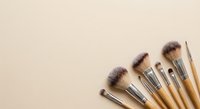 Professional makeup brushes with wooden handles arranged on neutral beige background for beauty and cosmetics applications.