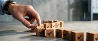 Business hand placing wooden blocks with checkmarks in row on desk representing task completion and project management success.
