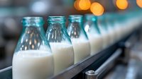 Fresh milk bottles on production line with bokeh lights in background, dairy factory manufacturing process showing quality control and automation.