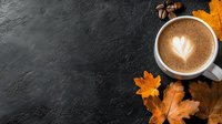 Hot cappuccino with heart latte art in white cup on dark concrete background with autumn maple leaves and acorns, copy space for seasonal menu.