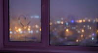 Heart drawn on foggy window glass with warm city lights bokeh background creating romantic evening atmosphere for Valentine's Day celebrations.