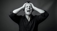 Young Caucasian man screaming with hands on head expressing extreme stress, frustration and mental breakdown in dramatic black and white portrait.