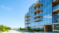 Modern residential apartment building with glass facade, wooden balconies and landscaping, suitable for real estate, architecture and urban development projects.