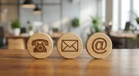 Three wooden contact icons on office desk showing phone, email and at symbol for business communication and customer service concepts.