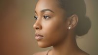Young African American woman with natural makeup and elegant earrings in profile view against warm neutral background for beauty and skincare concepts.