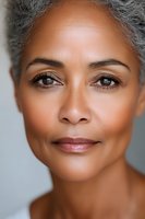 Close up portrait of mature African American woman with natural gray hair and gentle smile showing confidence and wisdom against light background.