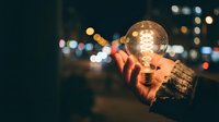 Hand holding glowing light bulb against blurred city lights at night, symbolizing innovation, creativity and bright ideas for business concepts.