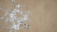 Water splash with droplets frozen in motion against neutral beige background. Dynamic liquid movement creates artistic patterns for refreshing beverage concepts.