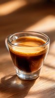 Fresh espresso shot with golden crema in double-wall glass on wooden surface, natural sunlight casting dramatic shadows, close-up view for coffee menu.