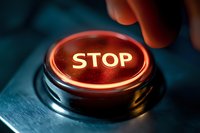 Glowing red stop button with finger hovering above, dramatic lighting on metallic surface creates urgent atmosphere for emergency concepts.