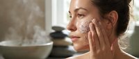 Young woman applying natural coffee scrub exfoliant to face during spa skincare routine at home for healthy glowing skin and anti-aging treatment.